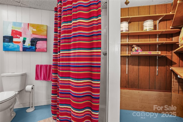 bathroom featuring toilet, concrete flooring, wooden walls, and curtained shower