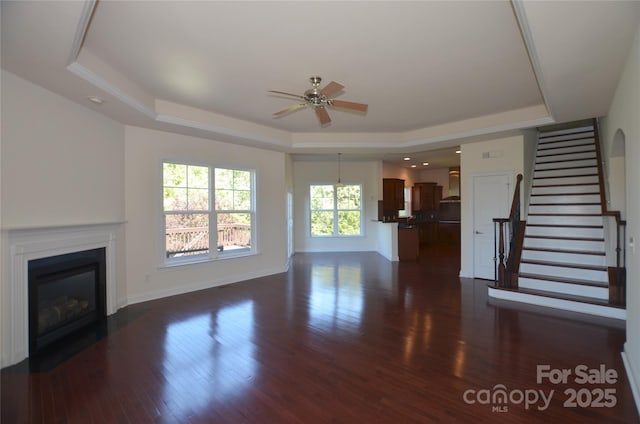 unfurnished living room featuring ceiling fan, dark wood-type flooring, and a tray ceiling