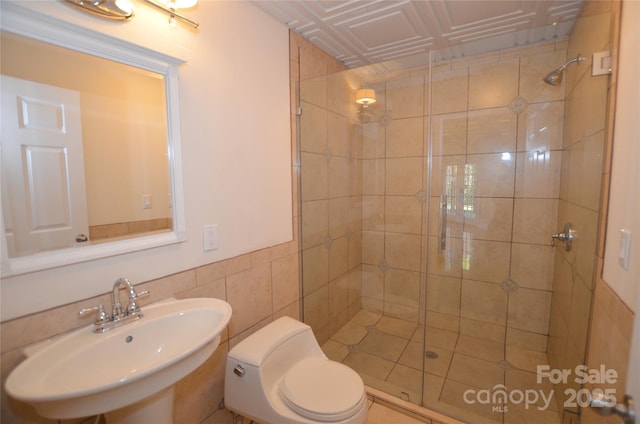 bathroom with tile walls, a shower with door, toilet, and sink