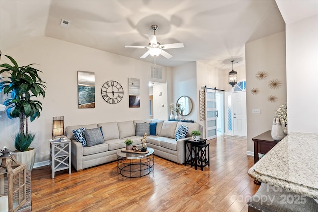 living room with ceiling fan, a barn door, lofted ceiling, and hardwood / wood-style flooring