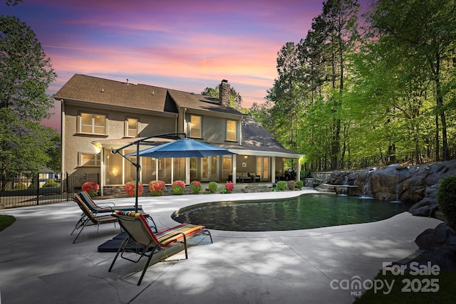 pool at dusk with a patio and pool water feature