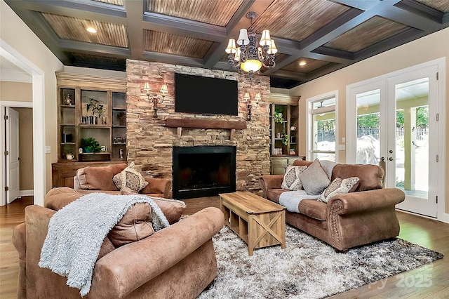 living room featuring a stone fireplace, hardwood / wood-style flooring, coffered ceiling, a notable chandelier, and french doors