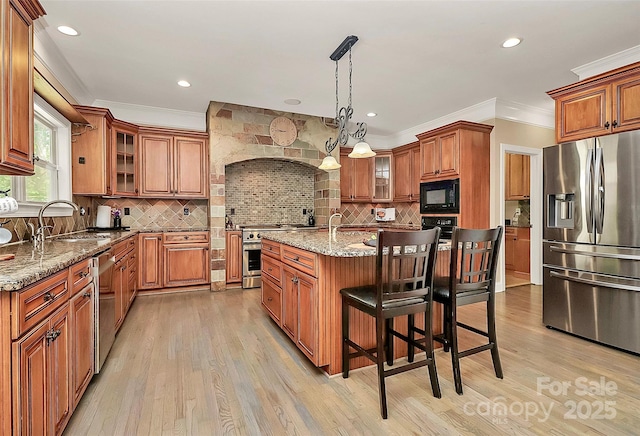 kitchen featuring pendant lighting, sink, stainless steel appliances, light stone countertops, and a center island with sink