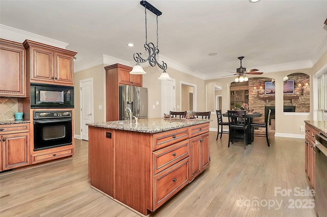 kitchen featuring black appliances, an island with sink, hanging light fixtures, light stone counters, and ceiling fan