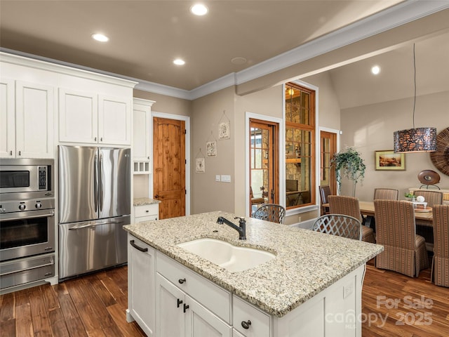 kitchen with sink, a kitchen island with sink, light stone countertops, stainless steel appliances, and white cabinets