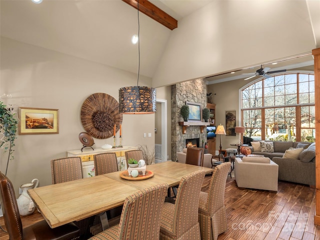 dining room with hardwood / wood-style flooring, a stone fireplace, ceiling fan, high vaulted ceiling, and beam ceiling