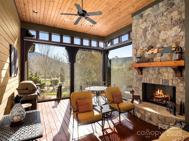 sunroom with ceiling fan, wooden ceiling, an outdoor stone fireplace, and a healthy amount of sunlight