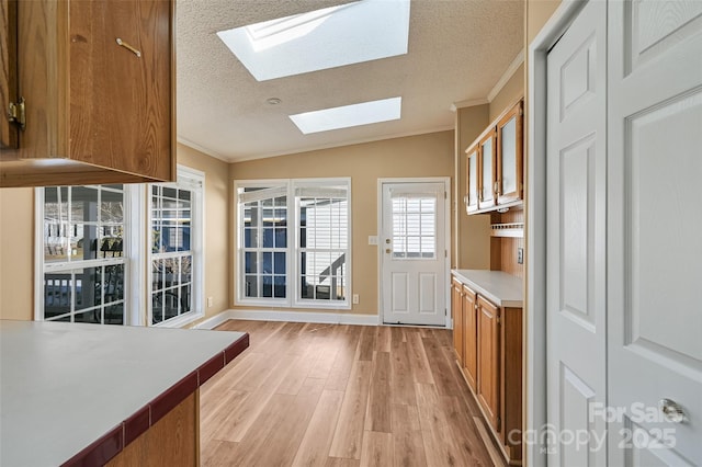 kitchen featuring a textured ceiling, lofted ceiling with skylight, crown molding, and light wood-type flooring