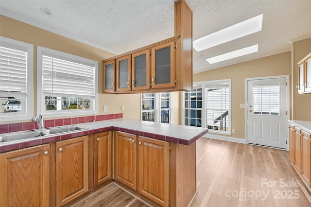 kitchen with light hardwood / wood-style floors, a textured ceiling, sink, lofted ceiling with skylight, and kitchen peninsula