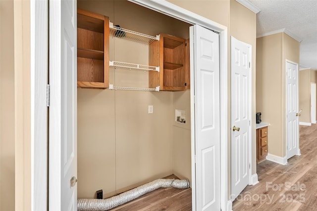 washroom featuring a textured ceiling, cabinets, washer hookup, light hardwood / wood-style flooring, and crown molding