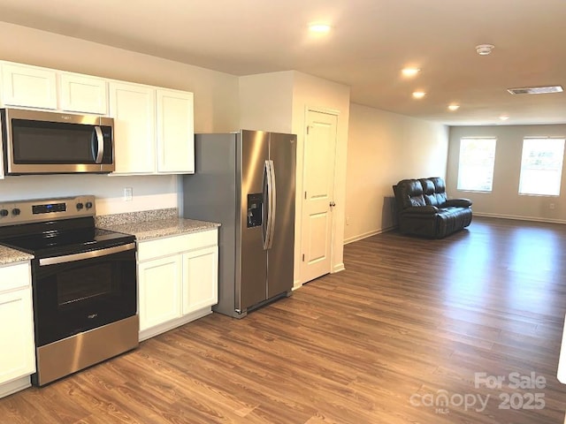 kitchen with light stone countertops, appliances with stainless steel finishes, dark hardwood / wood-style floors, and white cabinetry