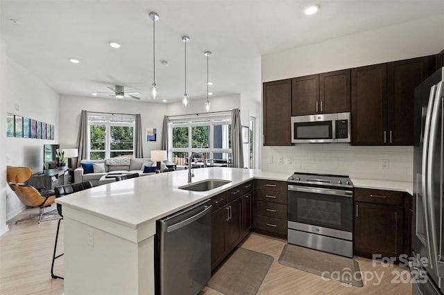 kitchen with stainless steel appliances, sink, a kitchen breakfast bar, backsplash, and ceiling fan