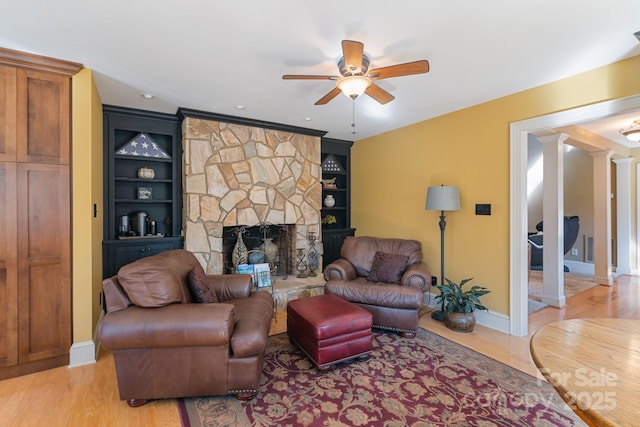 living room with built in shelves, ceiling fan, a stone fireplace, and decorative columns