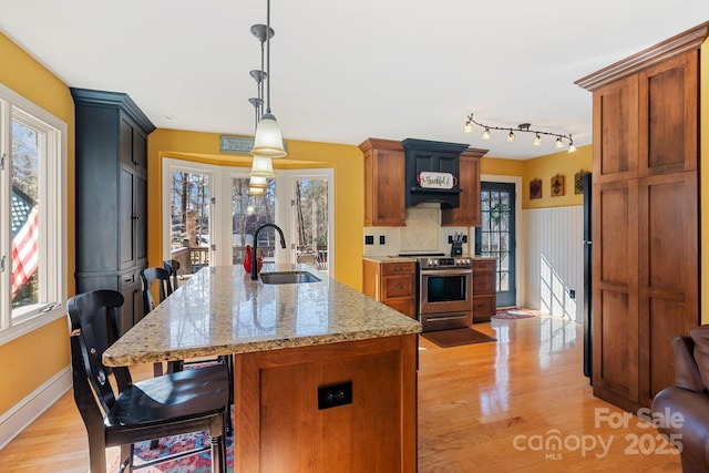 kitchen with sink, hanging light fixtures, electric range, light stone countertops, and an island with sink