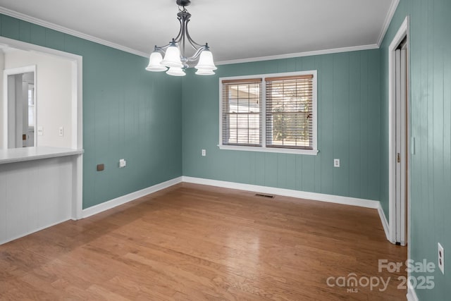 unfurnished dining area with crown molding, a chandelier, and hardwood / wood-style flooring