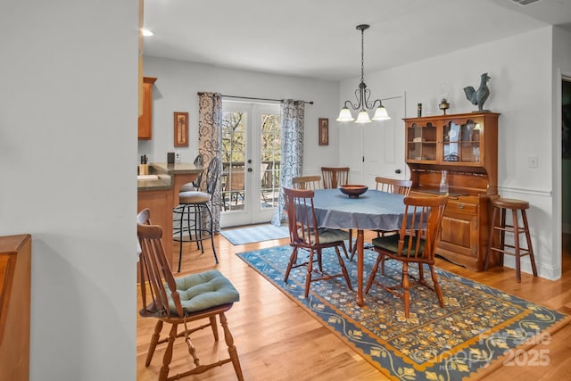 dining area featuring light wood-type flooring, french doors, and a chandelier