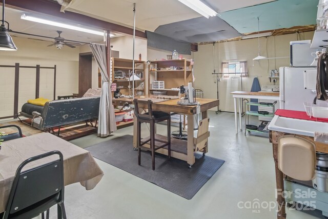 basement featuring white fridge, ceiling fan, and a workshop area