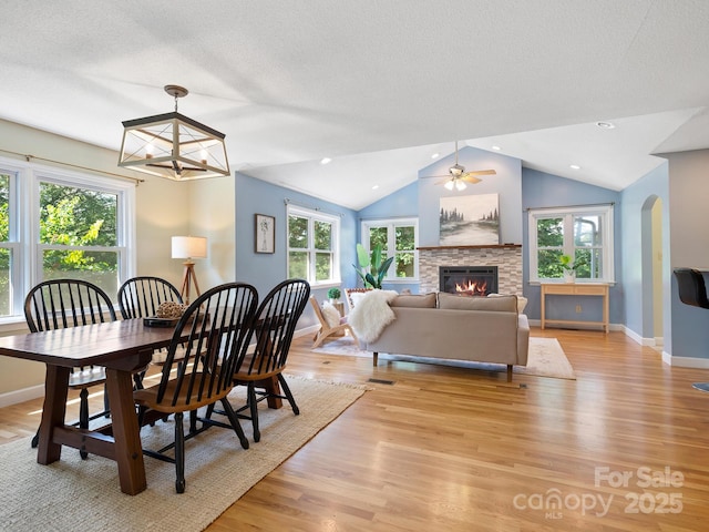 dining space featuring light hardwood / wood-style floors, ceiling fan, a stone fireplace, and vaulted ceiling