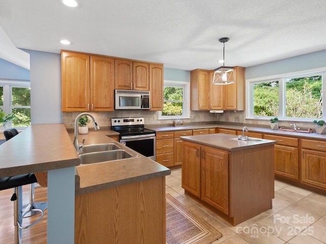 kitchen featuring decorative light fixtures, kitchen peninsula, decorative backsplash, sink, and stainless steel appliances