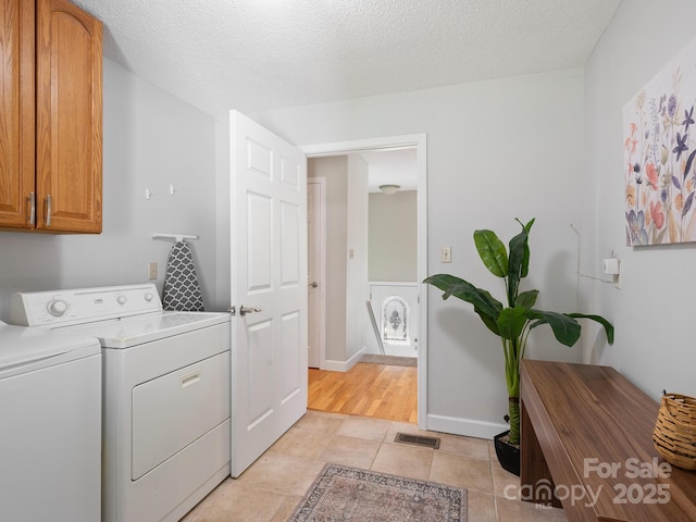 clothes washing area with light tile patterned floors, washing machine and dryer, a textured ceiling, and cabinets