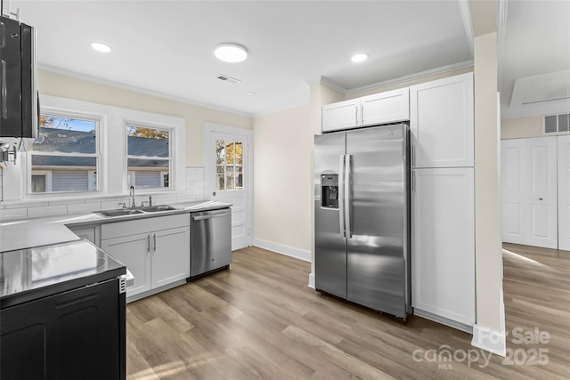 kitchen with appliances with stainless steel finishes, white cabinetry, sink, backsplash, and ornamental molding