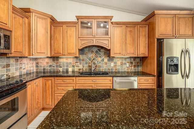 kitchen featuring lofted ceiling, stainless steel appliances, dark stone countertops, tasteful backsplash, and sink