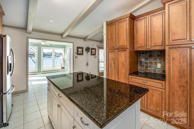 kitchen with white cabinetry, stainless steel fridge, decorative backsplash, dark stone countertops, and beamed ceiling