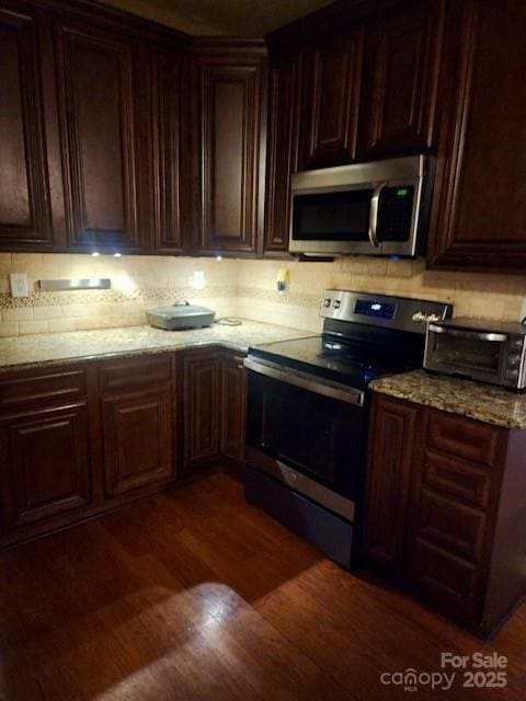 kitchen with light stone countertops, dark brown cabinetry, appliances with stainless steel finishes, and dark hardwood / wood-style flooring