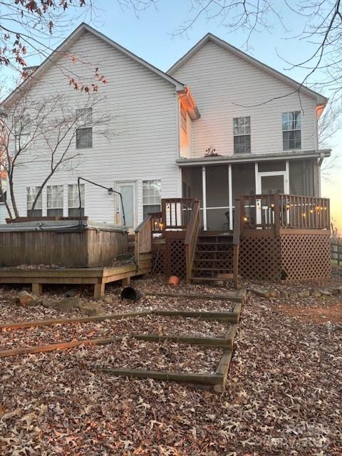 back house at dusk featuring a wooden deck and a sunroom