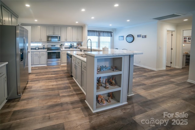 kitchen with dark wood-type flooring, a center island with sink, appliances with stainless steel finishes, ornamental molding, and sink