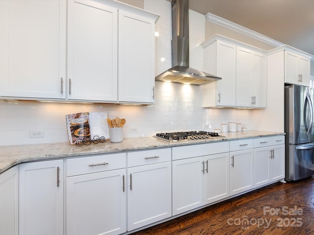 kitchen featuring stainless steel appliances, wall chimney range hood, white cabinets, and decorative backsplash