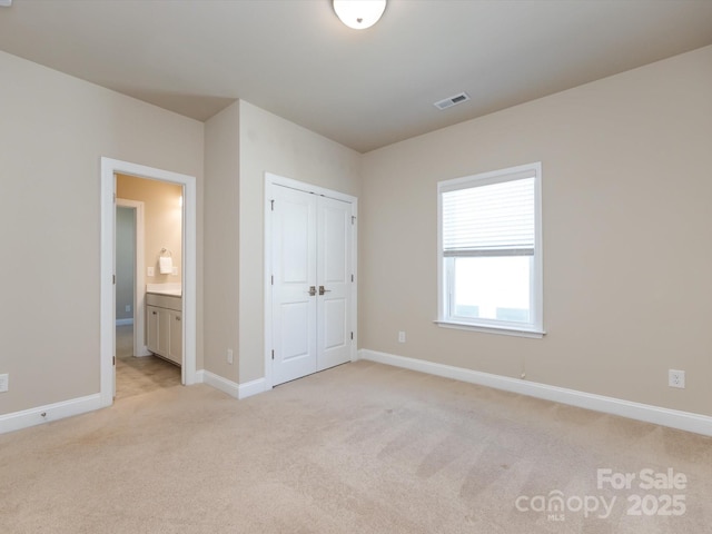 unfurnished bedroom with connected bathroom, light colored carpet, and a closet