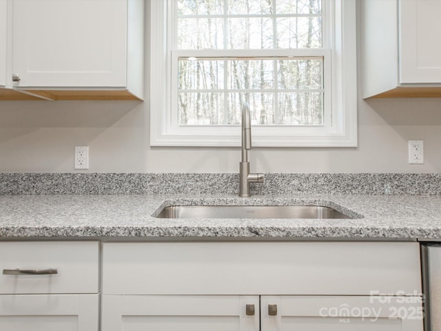 room details featuring white cabinets, sink, and light stone counters