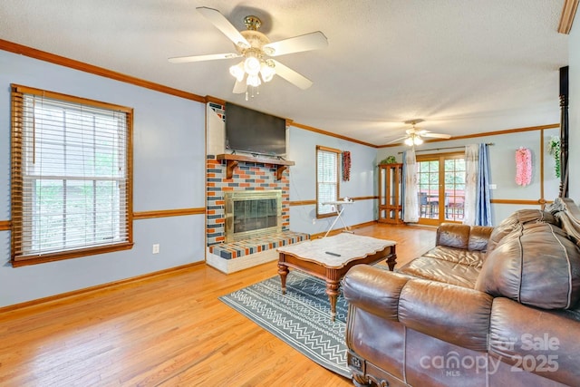 living room with light hardwood / wood-style floors, ceiling fan, ornamental molding, a brick fireplace, and a textured ceiling