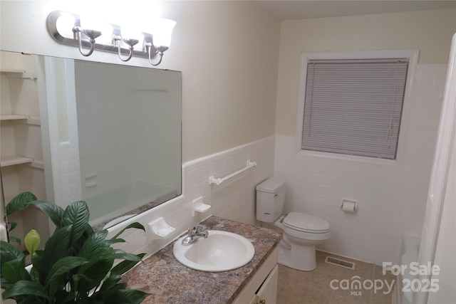 bathroom with toilet, tile patterned flooring, tile walls, and vanity