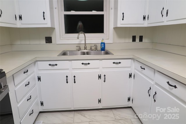 kitchen with white cabinetry, marble finish floor, light countertops, and a sink