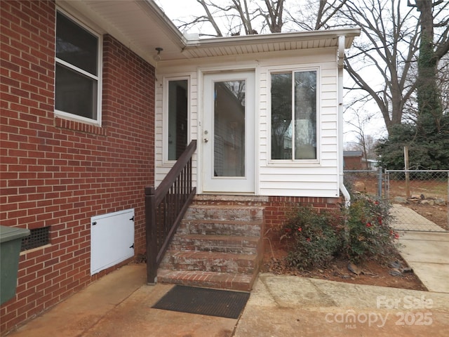 view of exterior entry with fence and brick siding