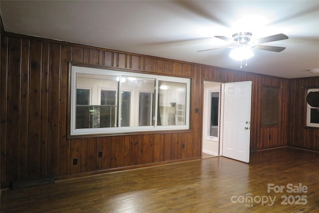 spare room with a ceiling fan, wood walls, baseboards, and wood finished floors