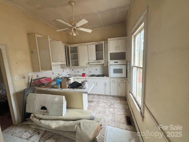 kitchen with white appliances, tile counters, ceiling fan, white cabinets, and backsplash