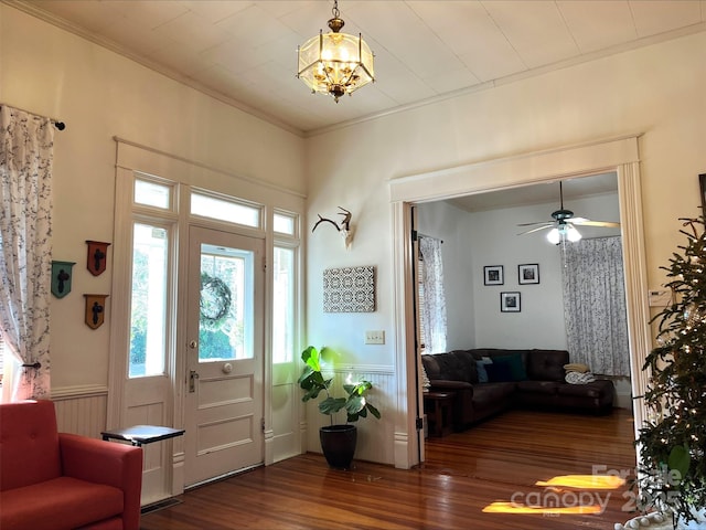 entrance foyer featuring dark wood-type flooring, ceiling fan with notable chandelier, and crown molding