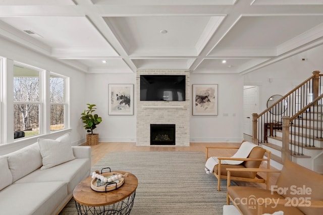 living room featuring coffered ceiling, stairway, light wood-type flooring, a fireplace, and beam ceiling