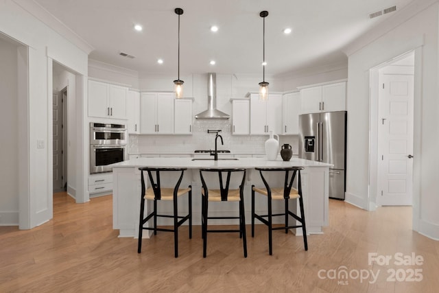 kitchen featuring wall chimney exhaust hood, appliances with stainless steel finishes, light countertops, and a kitchen island with sink