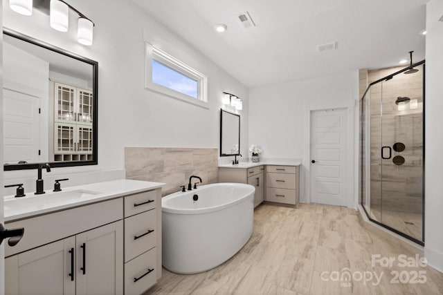 bathroom featuring two vanities, a sink, visible vents, a freestanding bath, and a stall shower