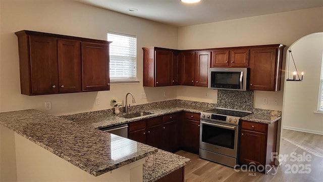 kitchen featuring kitchen peninsula, appliances with stainless steel finishes, dark stone countertops, light hardwood / wood-style flooring, and sink