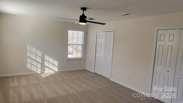 unfurnished bedroom with ceiling fan, light colored carpet, and multiple closets