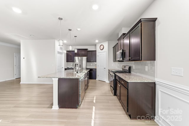 kitchen featuring light stone countertops, pendant lighting, appliances with stainless steel finishes, a center island with sink, and dark brown cabinets