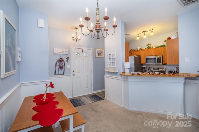 kitchen with a notable chandelier, pendant lighting, kitchen peninsula, appliances with stainless steel finishes, and light carpet