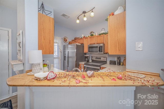 kitchen with hardwood / wood-style flooring, appliances with stainless steel finishes, kitchen peninsula, and wooden counters