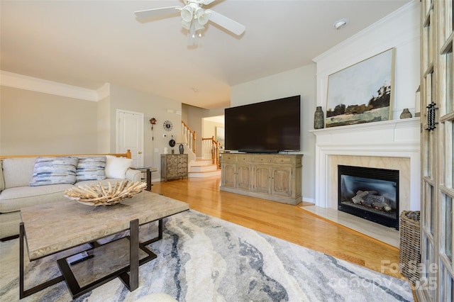 living room with ceiling fan, ornamental molding, light hardwood / wood-style floors, and a tile fireplace