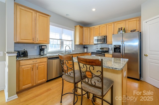 kitchen with appliances with stainless steel finishes, a center island, tasteful backsplash, light hardwood / wood-style floors, and light stone counters